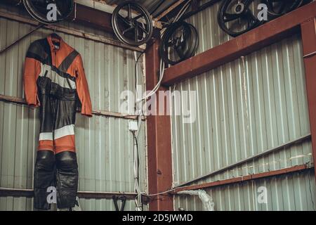 Des roues en alliage de moto et une combinaison de moto pendent sur un mur en métal dans un garage. Vente de roues de vélo de sport et vêtements en cuir, pantalons, veste dans un magasin Banque D'Images