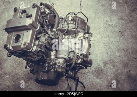 Vieux moteur de moto isolé dans un atelier, en gros plan. Un moteur en métal de motard repose sur un fond de ciment dans un garage. Placer pour le texte. Détails vintage Banque D'Images