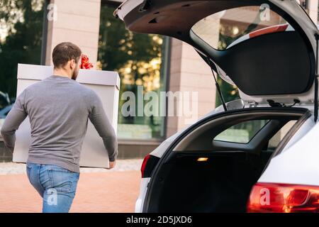 Vue arrière de l'homme de livraison prend grand blanc de fête boîte avec magnifique noeud rouge du coffre de la voiture Banque D'Images