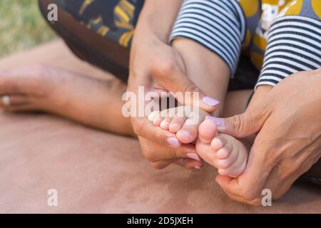 Les mains des mères maintiennent les jambes du bébé. Pieds nouveau-nés Banque D'Images