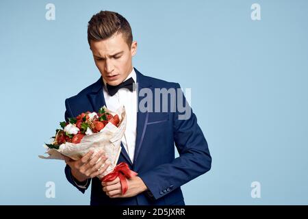 homme romantique avec un bouquet de fleurs et dans un noeud papillon sur fond bleu vue rognée Banque D'Images