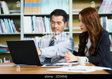 homme d'affaires et femme d'affaires asiatiques ayant une discussion dans le bureau avec ordinateur portable Banque D'Images