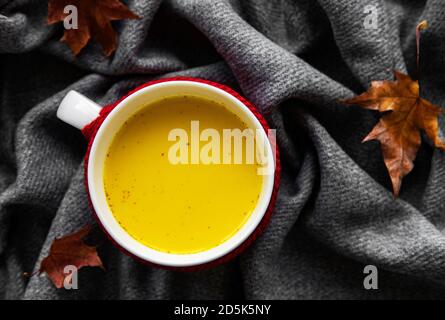 Lait doré dans une tasse blanche. Feuilles d'automne. Une boisson saine à base de lait, de curcuma, de cannelle et de miel. Banque D'Images