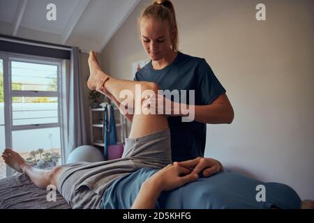 Belle jeune femme physiothérapeute donnant le traitement de jambe et de genou à patient en clinique Banque D'Images