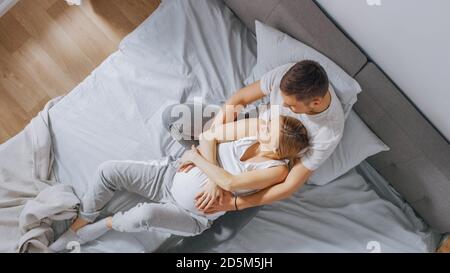 Un jeune couple heureux se câliner dans le lit, la jeune femme est enceinte et le mari affectueux la tient dans l'étreinte et caresse sa Belly tendly Banque D'Images