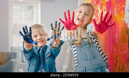 Deux petites sœurs amusantes montrent leurs mains qui sont plongées dans la peinture colorée. Ils sont heureux et rient. Objectifs de l'entreprise. Redécoration à la maison. Banque D'Images