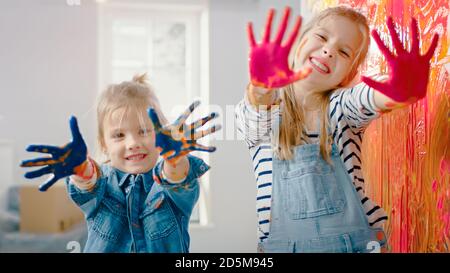 Deux petites sœurs amusantes montrent leurs mains qui sont plongées dans la peinture colorée. Ils sont heureux et rient. Objectifs de l'entreprise. Redécoration à la maison. Banque D'Images