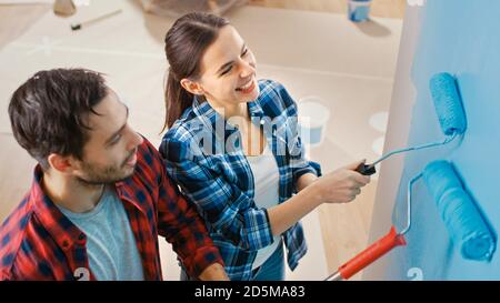 Jeune beau couple parler et décorer leur nouvel appartement. Mari et femme peint le mur avec des rouleaux qui sont trempés dans la peinture bleu clair Banque D'Images