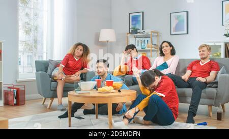 À la maison divers groupes de fans de sports portant le match de match de l'équipe de sport de montre uniforme sur la télévision, ils applaudissent mais l'équipe perd. Chambre confortable avec en-cas et Banque D'Images