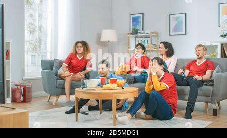 À la maison divers groupes de fans de sports portant le match de match de l'équipe de sport de montre uniforme sur la télévision, ils applaudissent mais l'équipe perd. Chambre confortable avec en-cas et Banque D'Images