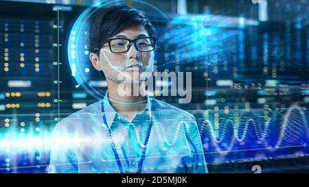 Jeune ingénieur INFORMATIQUE asiatique identifié par le processus de numérisation biométrique de reconnaissance faciale dans la salle de serveurs du centre de données. Concept futuriste : projecteur Banque D'Images