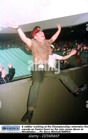 Un soldat qui travaille aux Championnats s'amuse à la foule Center court quand la pluie tombe à Wimbledon Banque D'Images