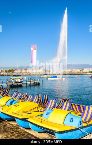 Pédalos alignés sur les rives du lac Léman à Genève, le matin d'été ensoleillé avec la fontaine jet d'eau Jet d'eau au loin. Banque D'Images