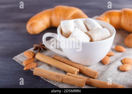 une tasse de chocolat chaud avec guimauve, croissants et épices sur serviette en lin et fond en bois noir. gros plan, espace copie. Banque D'Images