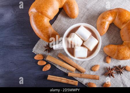 une tasse de chocolat chaud avec guimauve, croissants et épices sur une serviette en lin et un fond en bois noir. vue sur le dessus, espace copie. Banque D'Images