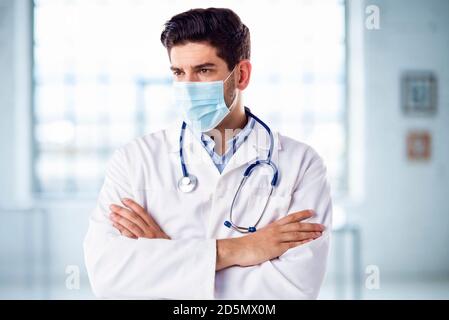 Portrait d’un médecin pensant portant un masque facial debout avec les bras croisés dans le foyer de l’hôpital. Banque D'Images