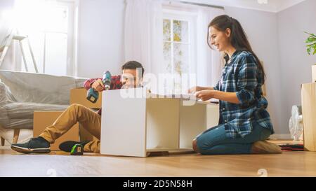 Le couple heureux assemble le mobilier en équipe, la fille lit les instructions et le garçon serre la vis avec une perceuse. Déménagement dans un nouvel appartement, couple Assemble Banque D'Images