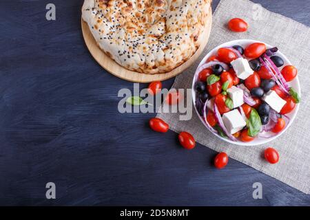 Salade grecque avec tomates cerises fraîches, fromage feta, olives noires, basilic et oignon sur fond de bois noir, crêpes, vue de dessus, espace copie. Banque D'Images