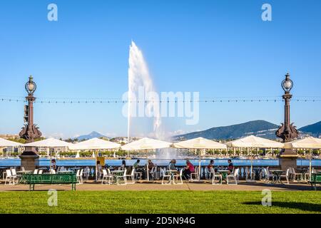 Touristes profitant de la terrasse ensoleillée d'un glacier près de la baie de Genève, avec vue panoramique sur la fontaine à jet d'eau et le Mont blanc. Banque D'Images