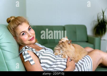Femme blonde enceinte couchée sur le canapé avec un chat. Banque D'Images