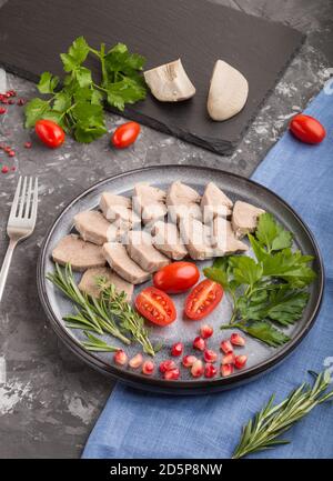 Langue de porc bouillie avec tomates et herbes sur fond de béton noir et tissu de lin bleu. Vue latérale, gros plan. Banque D'Images