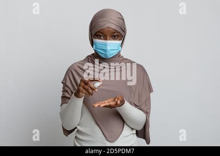 Précautions contre le coronavirus. Femme musulmane noire en masque appliquant un spray désinfectant sur les mains Banque D'Images