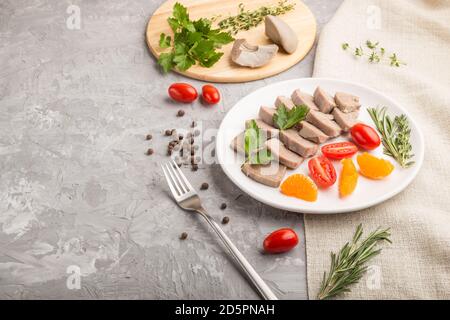 La langue de porc bouillie avec des tomates et des herbes sur fond de béton gris et le tissu de lin. Vue latérale, espace de copie. Banque D'Images