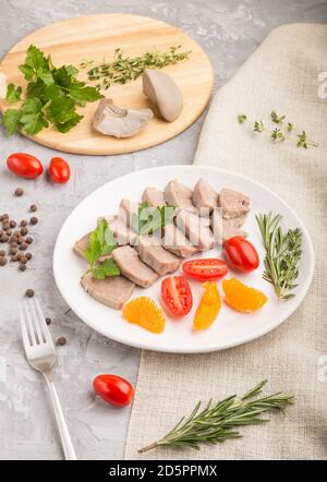 La langue de porc bouillie avec des tomates et des herbes sur fond de béton gris et le tissu de lin. Vue latérale, gros plan. Banque D'Images