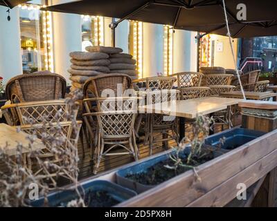 Une pile de chaises de rue en rotin et de tables le soir d'automne à la lumière des fenêtres du magasin. Fin de saison dans un café de rue de Moscou. Démontage de Banque D'Images