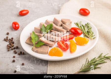 La langue de porc bouillie avec des tomates et des herbes sur fond de béton gris et le tissu de lin. Vue latérale, gros plan, mise au point sélective. Banque D'Images