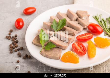 La langue de porc bouillie avec des tomates et des herbes sur fond de béton gris et le tissu de lin. Vue latérale, gros plan, mise au point sélective. Banque D'Images