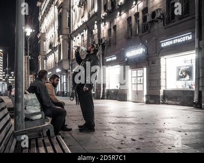 Moscou. Russie. Le 13 octobre 2020 UN groupe d'hommes sur un banc lors d'une soirée d'automne. L'homme a renvoyé sa tête boit de l'eau d'une bouteille. Fenêtres de magasin Banque D'Images