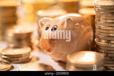 La banque de porc se tient entre des piles de pièces Banque D'Images