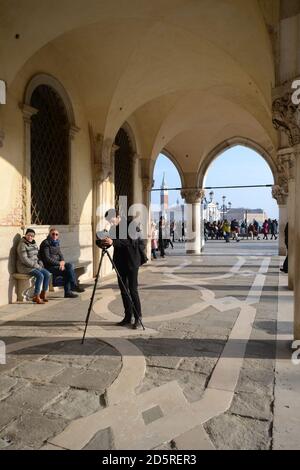 le photographe place l'appareil photo sur le trépied sous un portique sur la piazza san marco Banque D'Images
