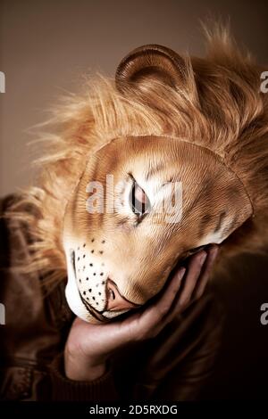 portrait d'un homme portant un masque de lion soutenant sa tête dans sa main, sur fond beige, avec un traitement rétro Banque D'Images