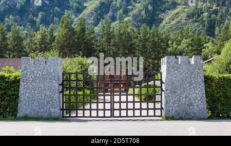 Entrée stylisée du centre de loisirs par la porte du château avec colonnes en pierre et barres de fer avec arbres verts et une maison en bois sous le moun Banque D'Images