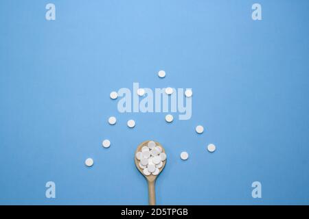 Comprimés blancs ronds, comprimés avec une cuillère en bois pleine de comprimés sur fond bleu, isolés Banque D'Images