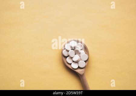 comprimés blancs ronds sur une cuillère en bois sur fond jaune, la cuillère est située au centre de bas en haut, isoler. Banque D'Images