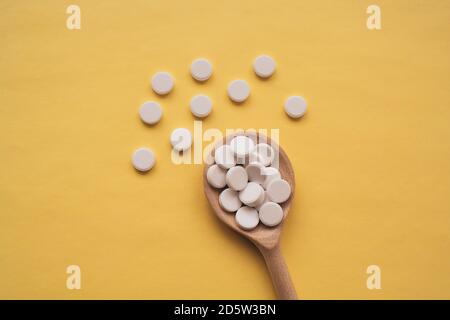 Comprimés blancs ronds sur une cuillère en bois sur fond jaune, les comprimés sont dispersés au centre de bas en haut Banque D'Images