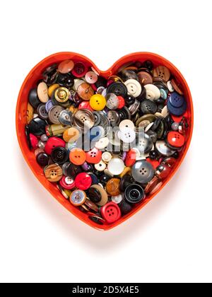 Boîte en plastique en forme de cœur remplie de boutons, vue de dessus, isolée sur fond blanc Banque D'Images