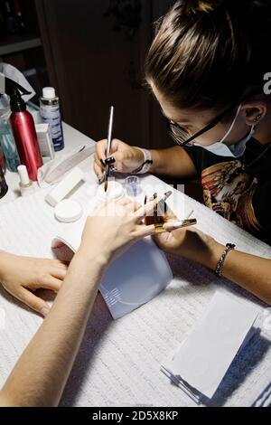 De dessus la femme dans le masque faisant la manucure française à la récolte client pendant une pandémie Banque D'Images