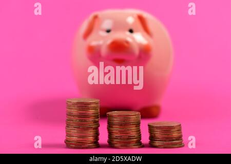 La piggy Bank se trouve à côté de piles de pièces. Cochon en céramique avec de l'argent à côté sur fond rose, défoqué. Investissement et croissance des revenus. Concept de planification budgétaire et de croissance des revenus Banque D'Images