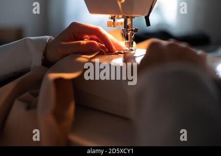 Anonyme femme couture vêtement sous éclairage sur machine dans l'obscurité studio à domicile Banque D'Images