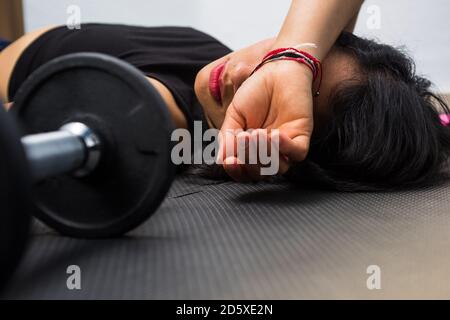 Gros plan photographie de la jeune femme se reposant après avoir fait de l'exercice à la salle de gym, soutient le bras sur sa tête, concept de mal de tête. Banque D'Images