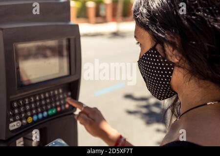 Détail d'une femme portant un masque facial de protection à l'aide d'une machine de stationnement dans la rue. Protection contre les coronavirus dans le nouveau transport normal, privé Banque D'Images