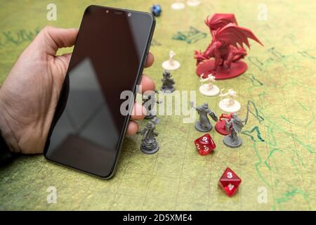 Utilisation du smartphone pendant un jeu de rôle de donjons et dragons. Dés et miniatures sur le champ de bataille vert du jeu. Écran noir avec Banque D'Images