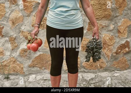 Basse section de fermier femelle tenant des tomates et des raisins pendant debout Banque D'Images