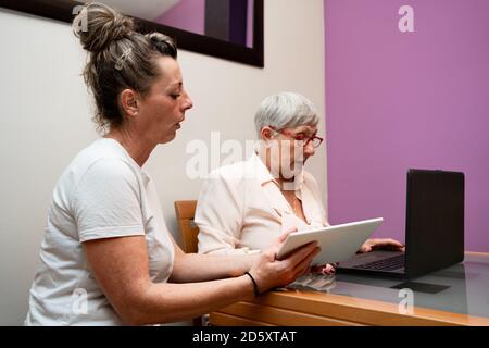 Femme caucasienne âgée et femme d'âge moyen assise à la maison au travail Banque D'Images