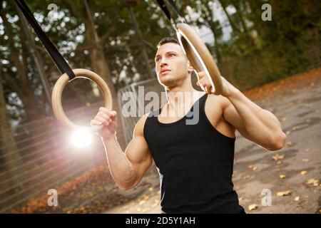 Jeune homme musclé de la formation sur les anneaux de gymnastique Banque D'Images