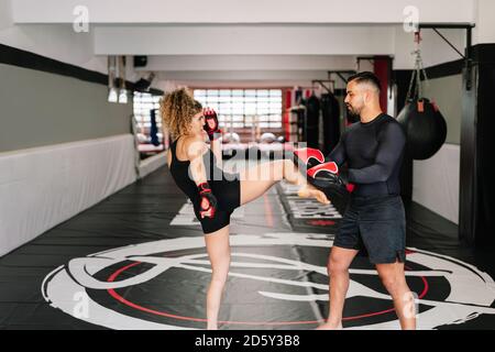 boxer féminin avec son entraîneur très concentré de rouge gants de boxe donnant directement un coup de pied sur les mains de l'entraîneur dans un salle de sport Banque D'Images